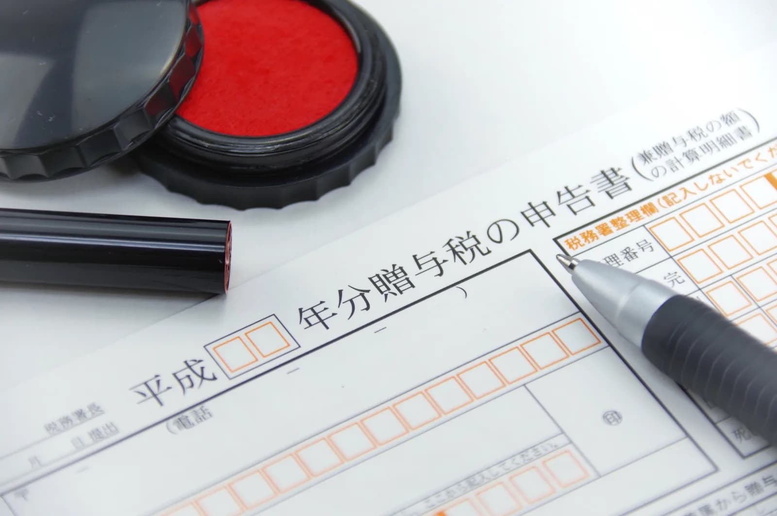 贈与税の申告書とボールペンと朱肉（個人間の無償譲渡と贈与税に関する記事のイメージ）