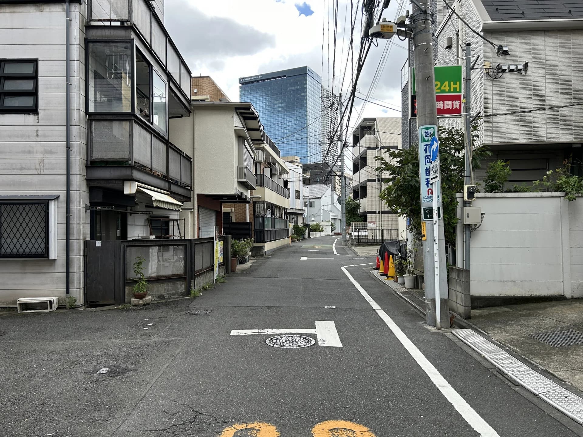 戸建てと低層住宅が並ぶ住宅地の路地の先に高層ビルが見える風景（中野区の空き家買取のイメージ）