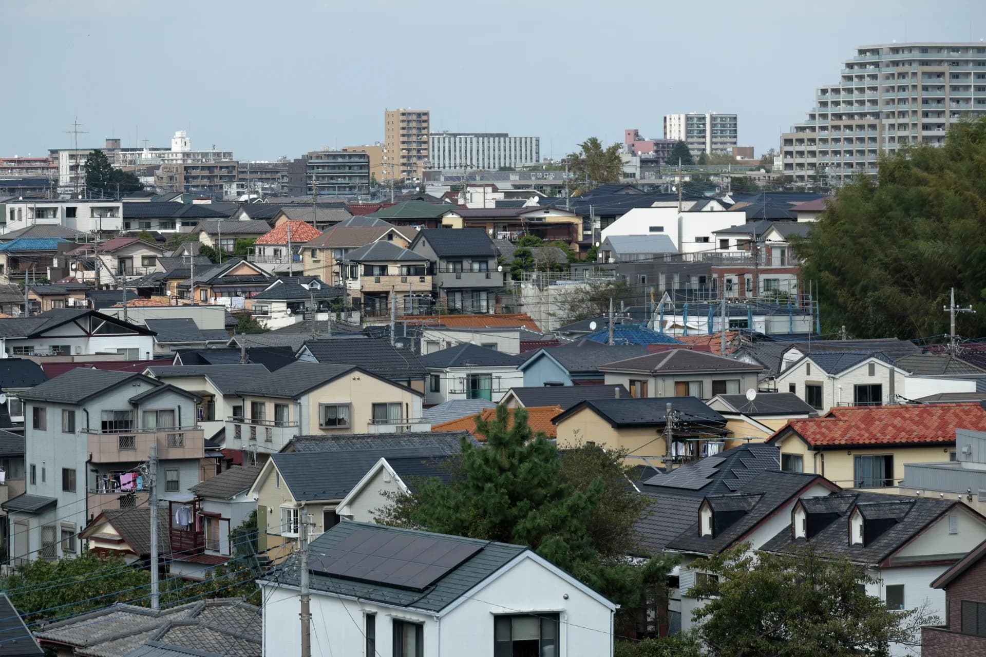 瓦屋根やスレート屋根の戸建て住宅が斜面に密集し奥にマンションが見える郊外の住宅街（西東京市の空き家買取のイメージ）