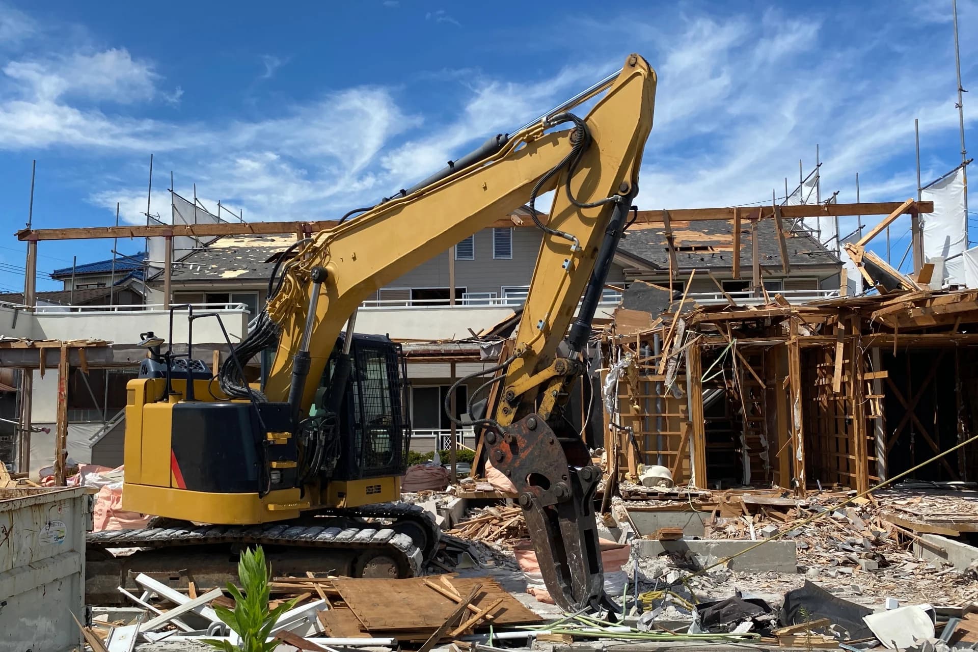 黄色い油圧ショベルが骨組みだけになった木造住宅を取り壊している解体現場