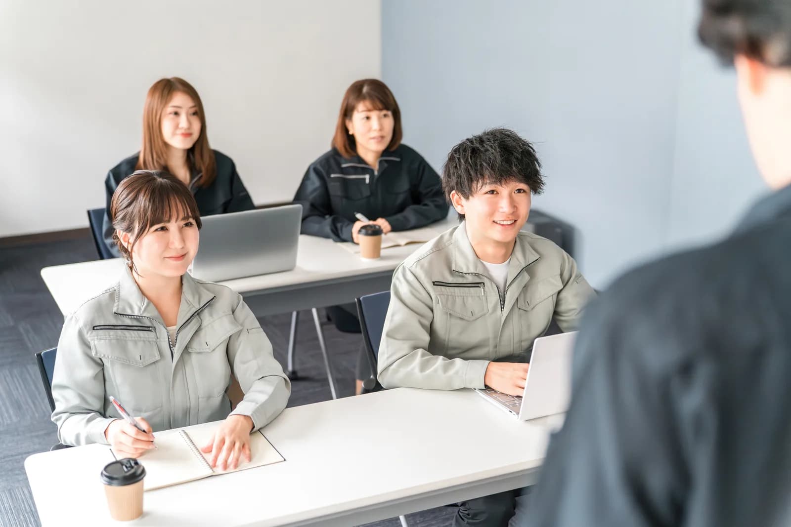 プレゼンを聞く作業着姿のビジネスマン男女(不動産買取業者に関する記事のイメージ)