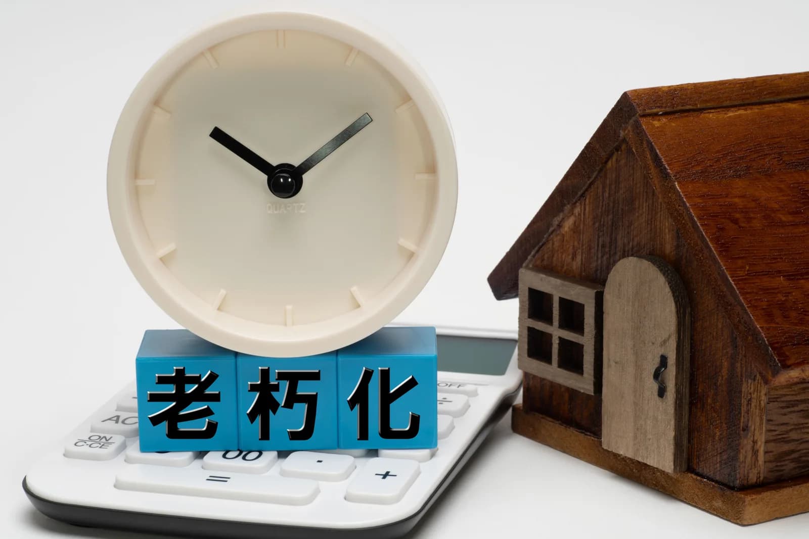 目覚まし時計と電卓と家の模型と「老朽化」の文字ブロック(いらない家の維持費に関する記事のイメージ)