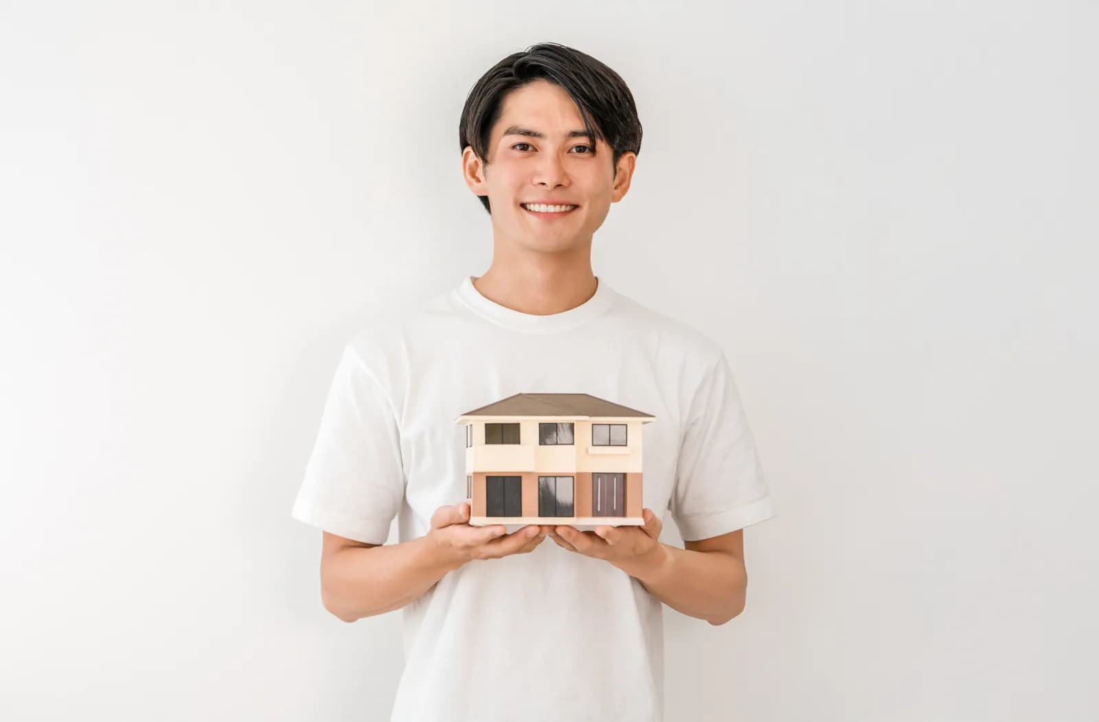 住宅模型を持つ笑顔の若いアジア人男性(共有持分に関する記事のイメージ)