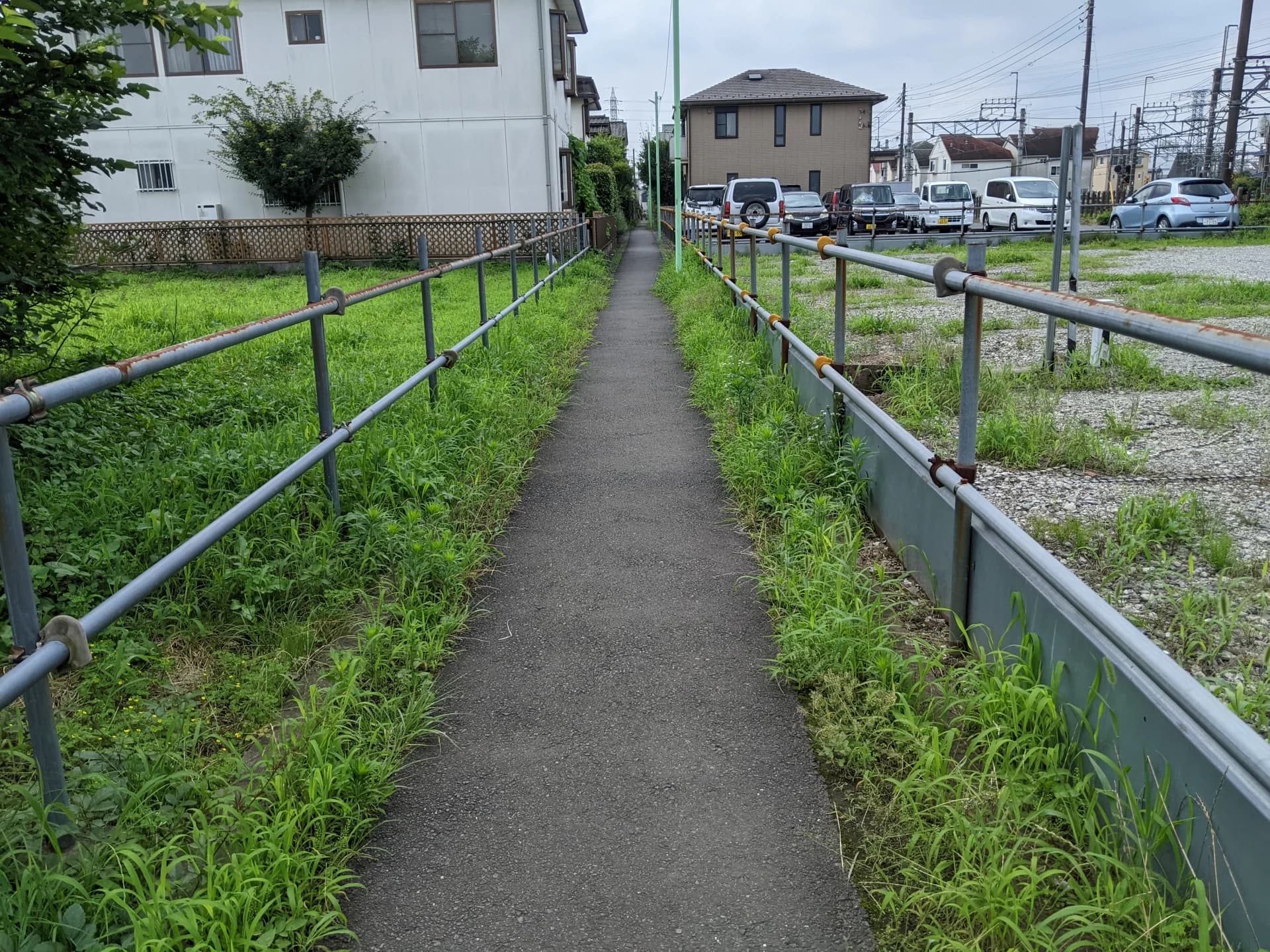 空き地の間を抜ける手すり付きの細い舗装通路(隣の土地を通る地役権のイメージ)