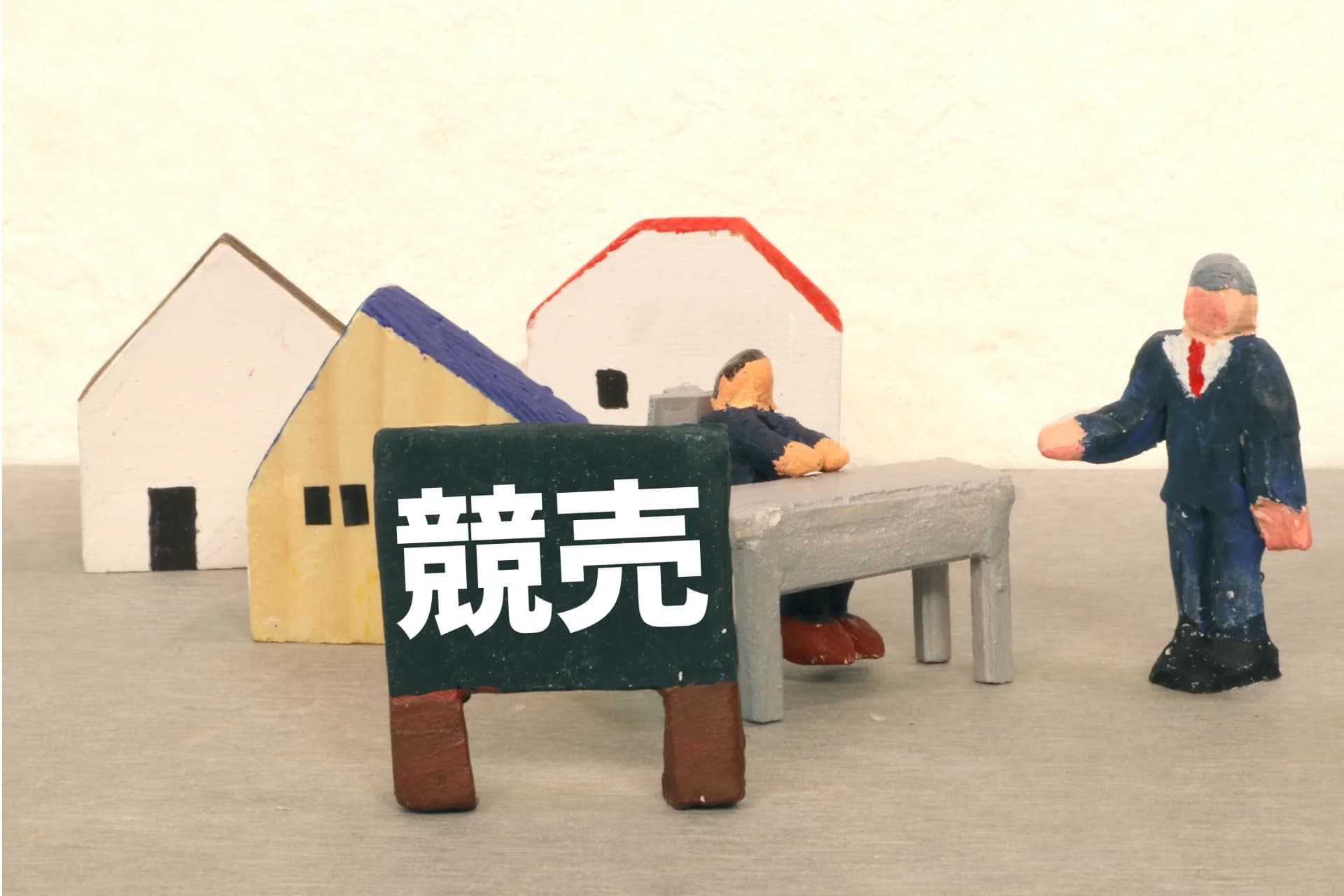 「競売」と書かれた看板と家の模型、机に着く人形の置物(土地の競売と法定地上権のイメージ)