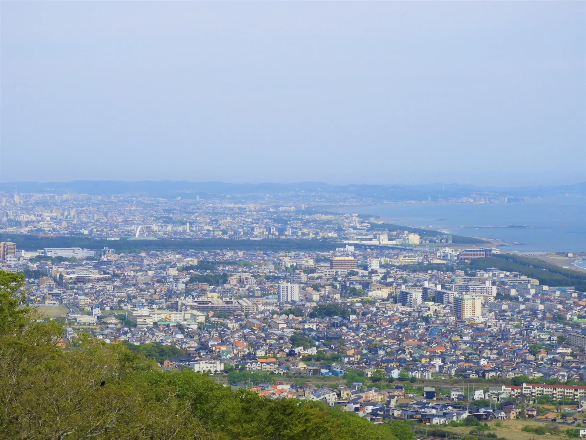 湘南平から見下ろした平塚・茅ヶ崎方面の市街地に戸建て住宅が広がり、右奥に相模湾の海岸線が続く眺め(茅ヶ崎市の空き家買取のイメージ)