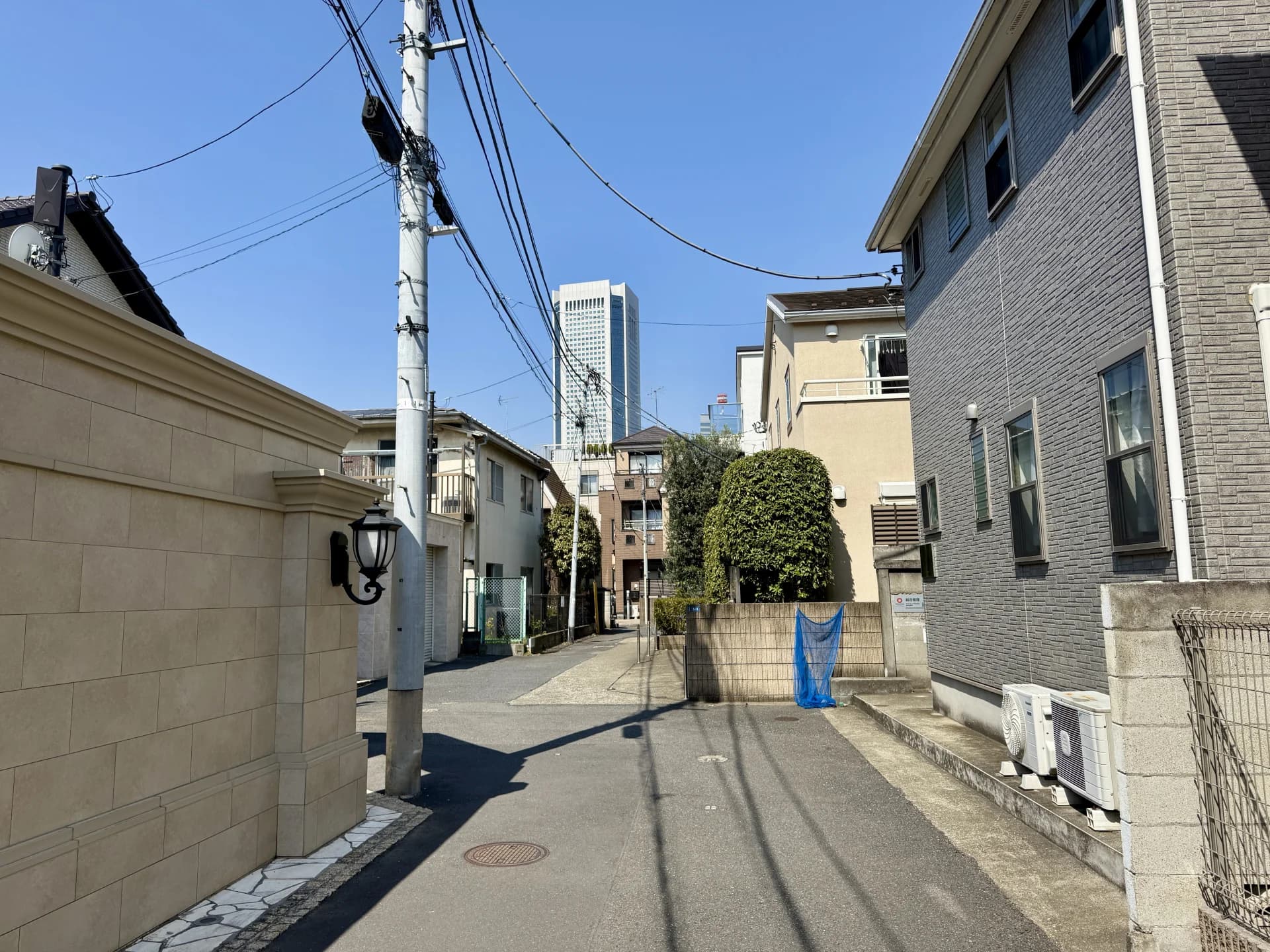 代々木の住宅街で戸建てに挟まれた路地の先に高層ビルが見える風景(渋谷区の空き家買取のイメージ)