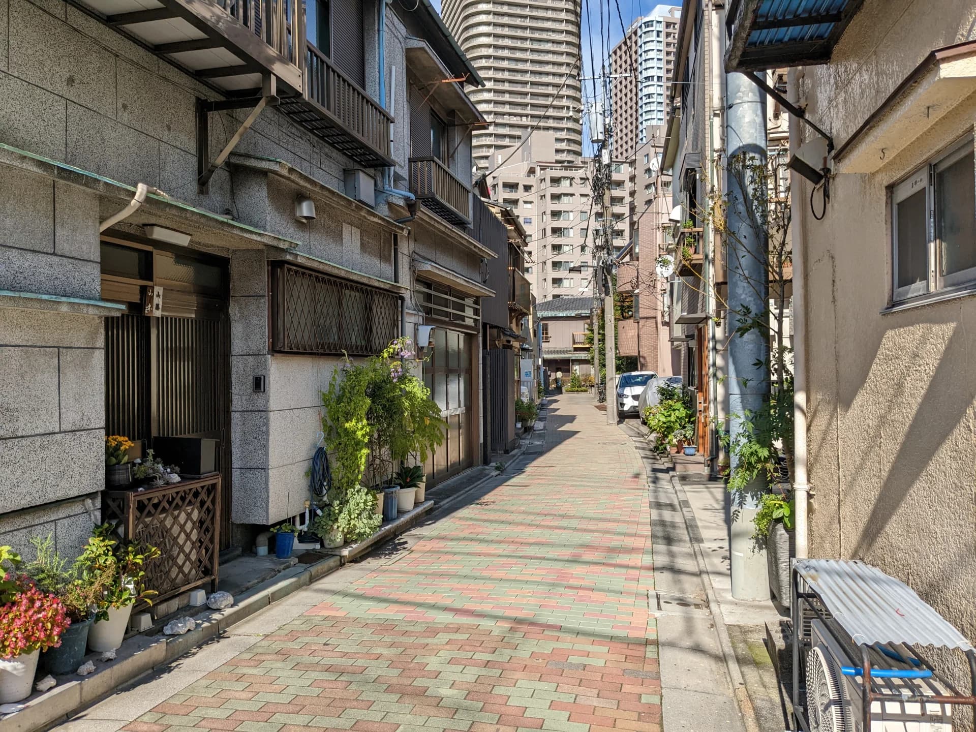 佃島の路地に古い木造住宅が連なり、奥にタワーマンションが見える街並み(中央区の空き家買取のイメージ)