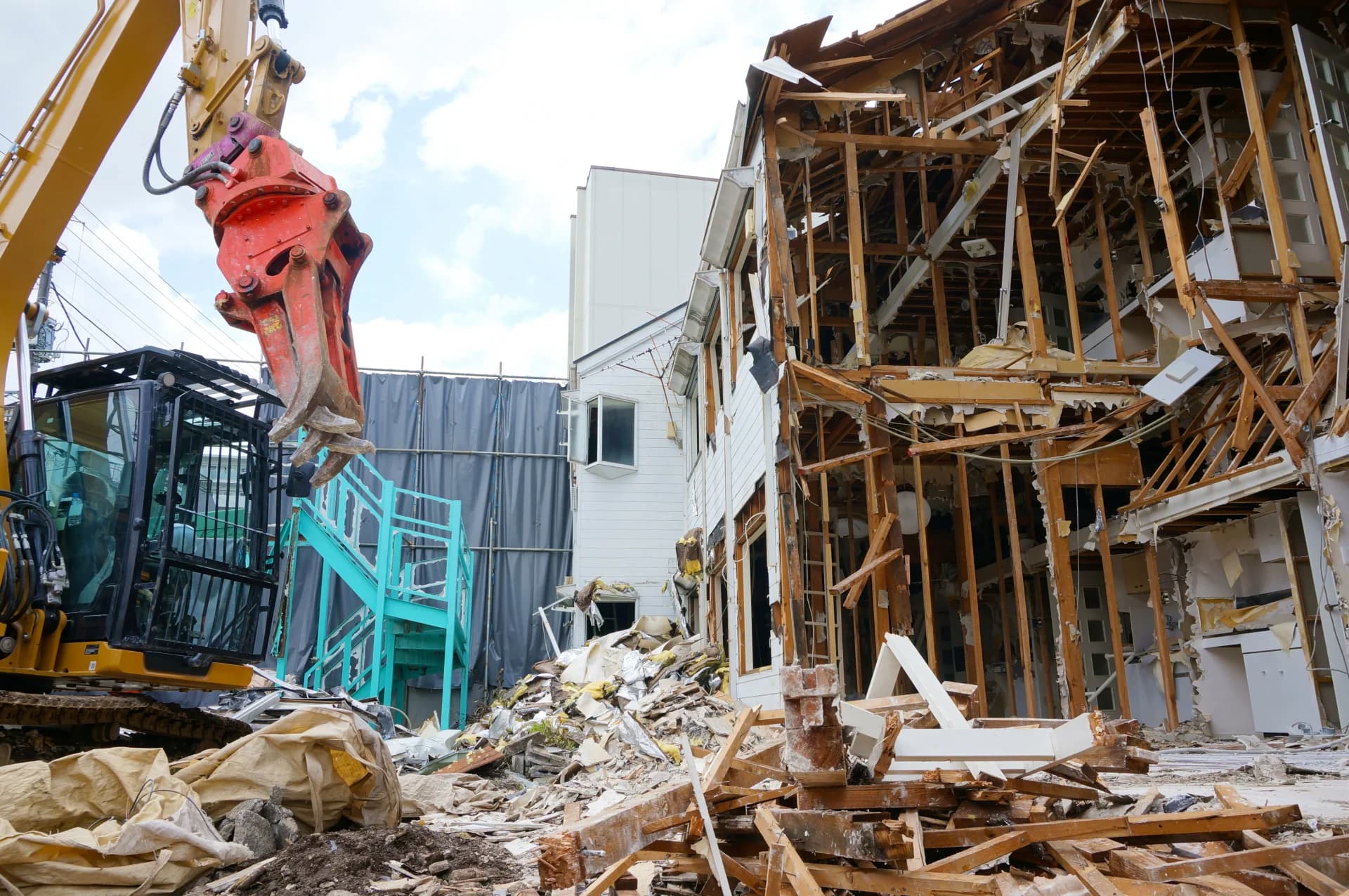 骨組みがむき出しになった木造2階建ての建物を、重機で取り壊している解体現場(家の解体費用のイメージ)