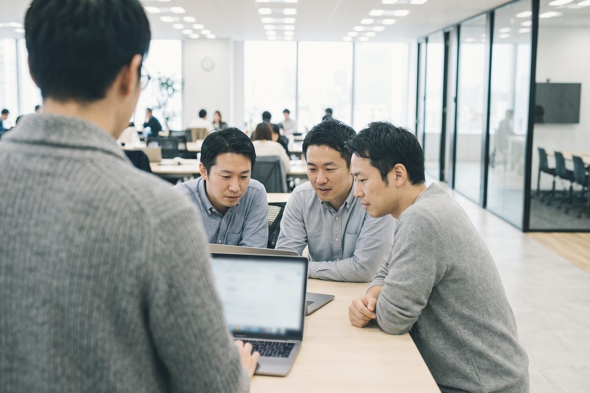 1台のノートパソコンの画面を囲んで見ている3人。手前に後ろ姿の1人と、図を描いた紙
