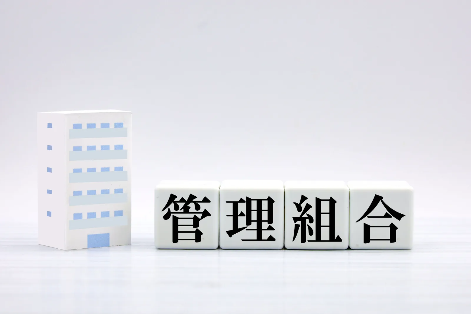 マンションの模型と「管理組合」の文字ブロック(親のマンションの処分に関する記事のイメージ)