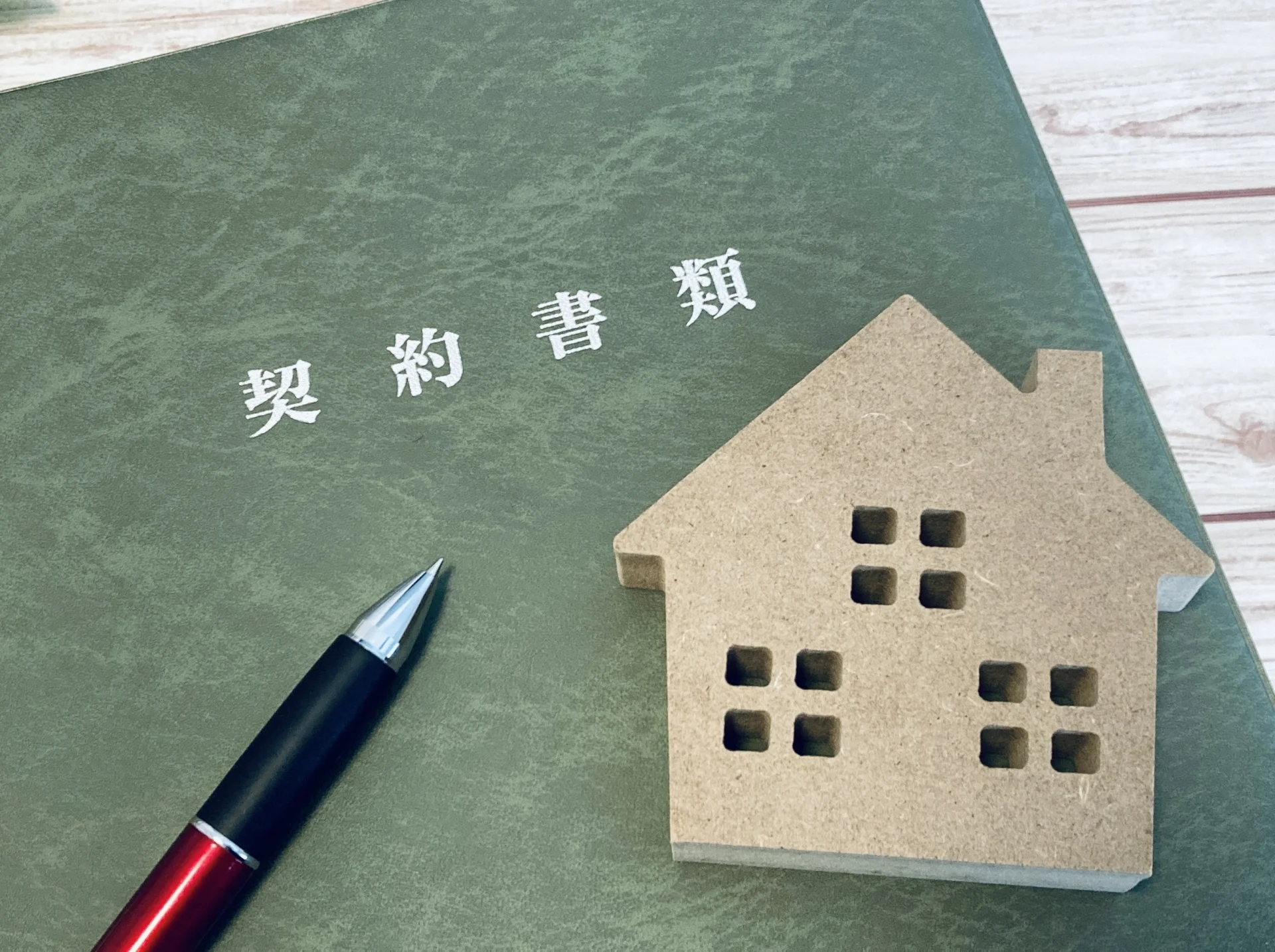 「契約書類」と書かれたファイルと木製の家の模型とペン(埼玉県の底地の買取のイメージ)