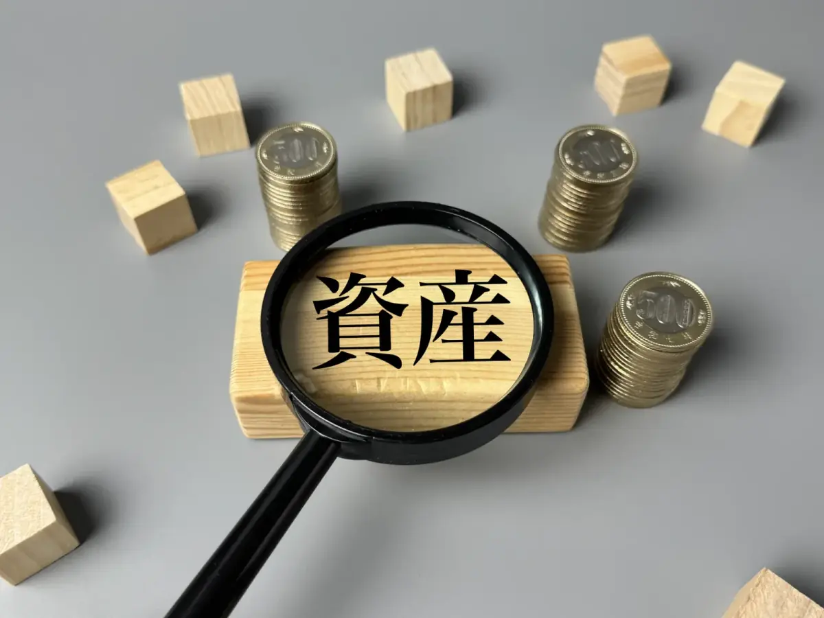 資産イメージ｜虫眼鏡と小銭と木のブロック（空き家に関する記事のイメージ）