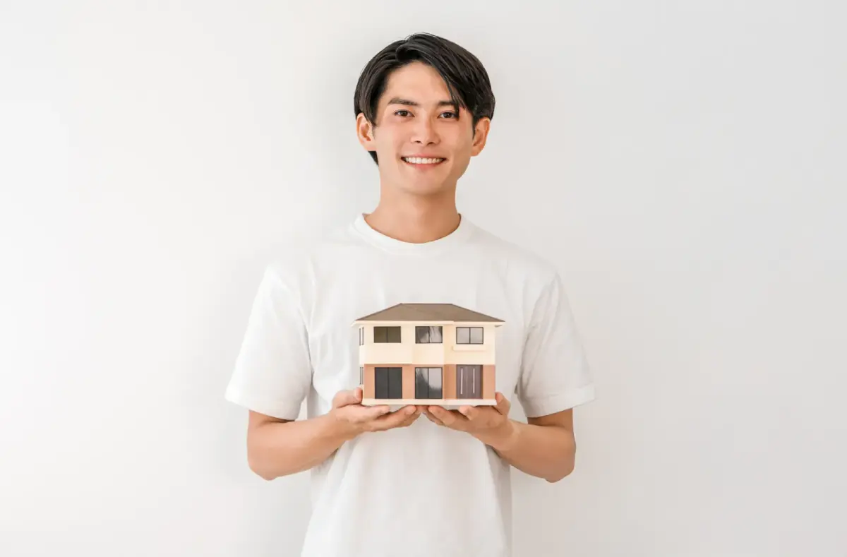 住宅模型を持つ笑顔の若いアジア人男性(共有持分に関する記事のイメージ)