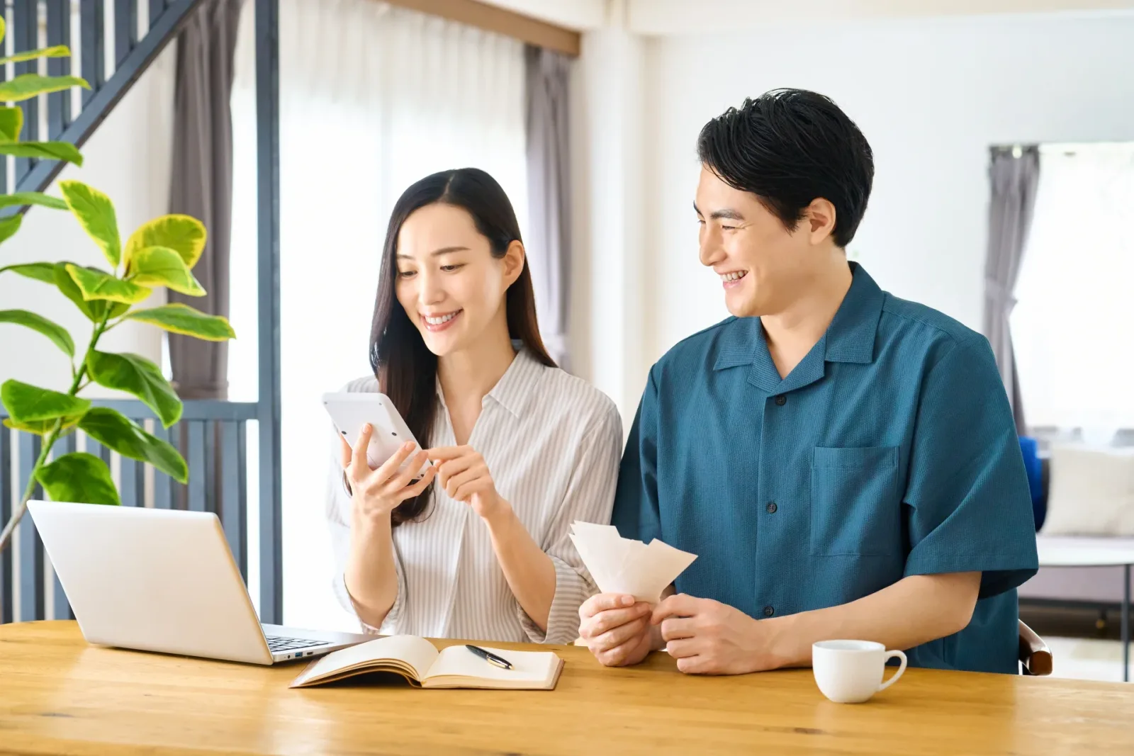スマホと電卓で笑顔で家計を管理する夫婦(空き家に関する記事のイメージ)