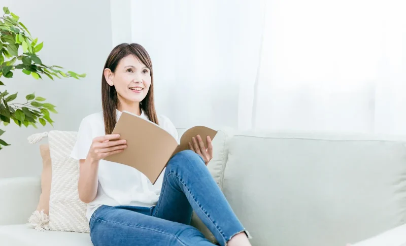 ソファに座るミドル世代の女性（ノート）（不動産売却に関する記事のイメージ）