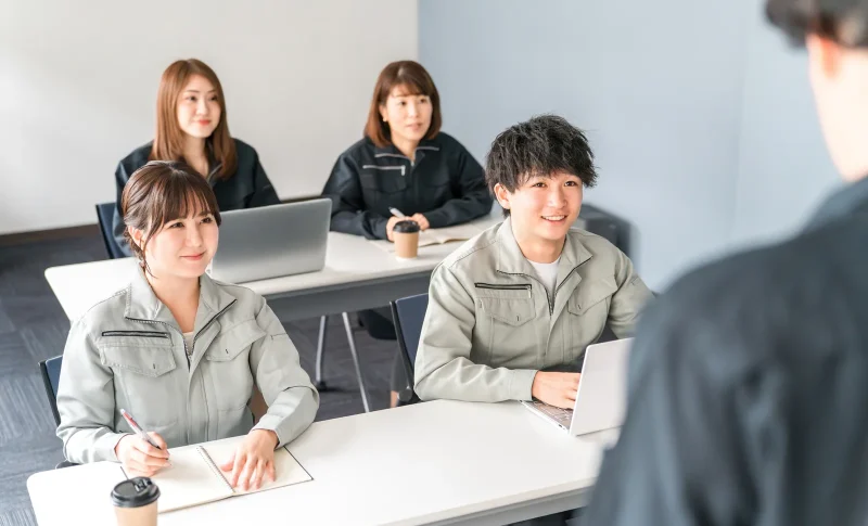 プレゼンを聞く作業着姿のビジネスマン男女（不動産買取業者に関する記事のイメージ）