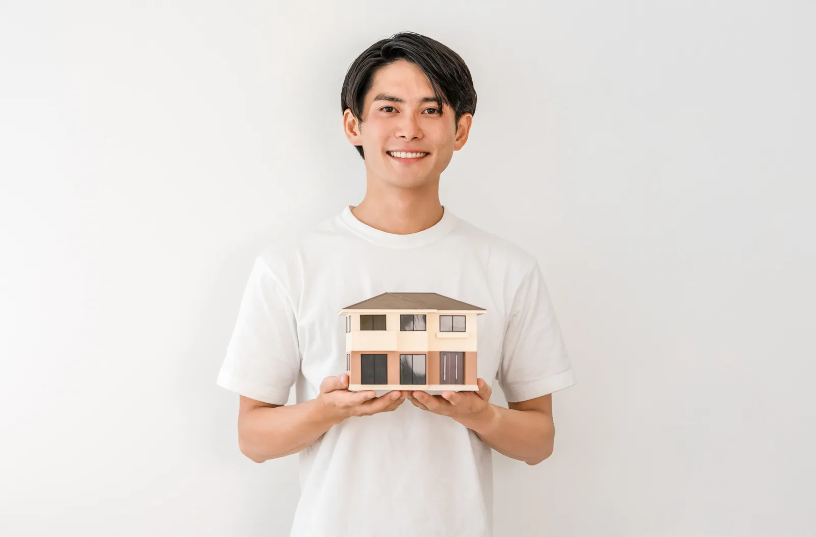 住宅模型を持つ笑顔の若いアジア人男性(共有持分に関する記事のイメージ)