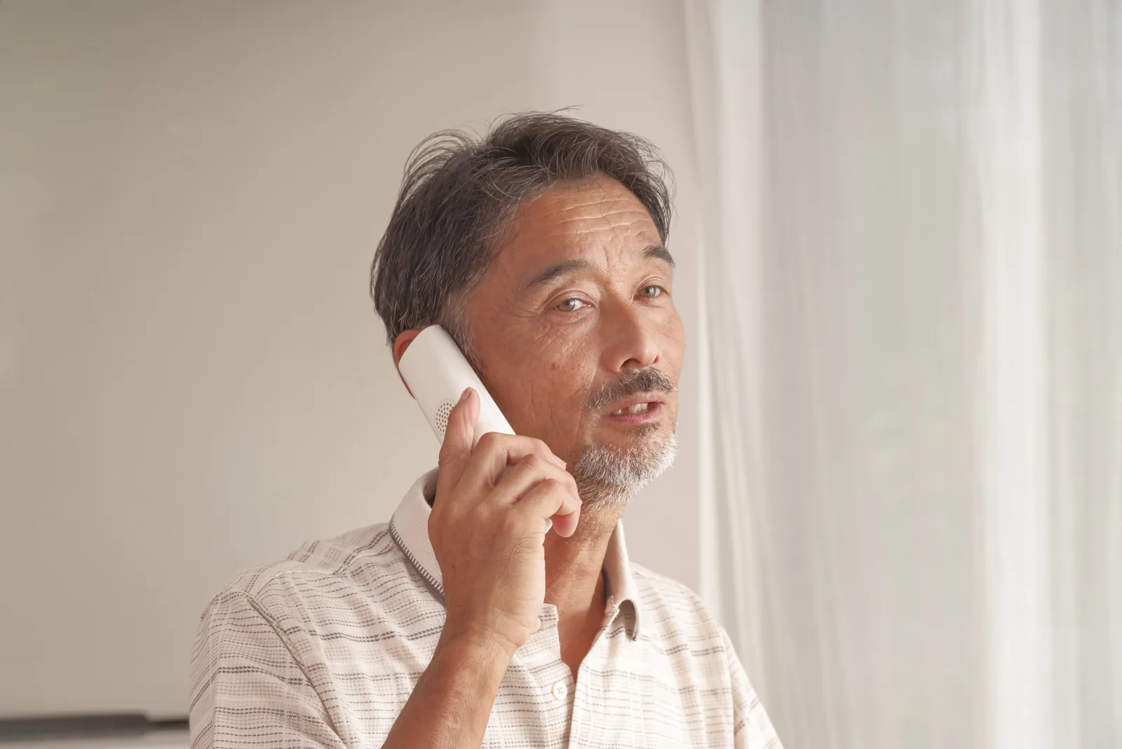 自宅で固定電話を使って通話するシニア男性(不動産売却に関する記事のイメージ)