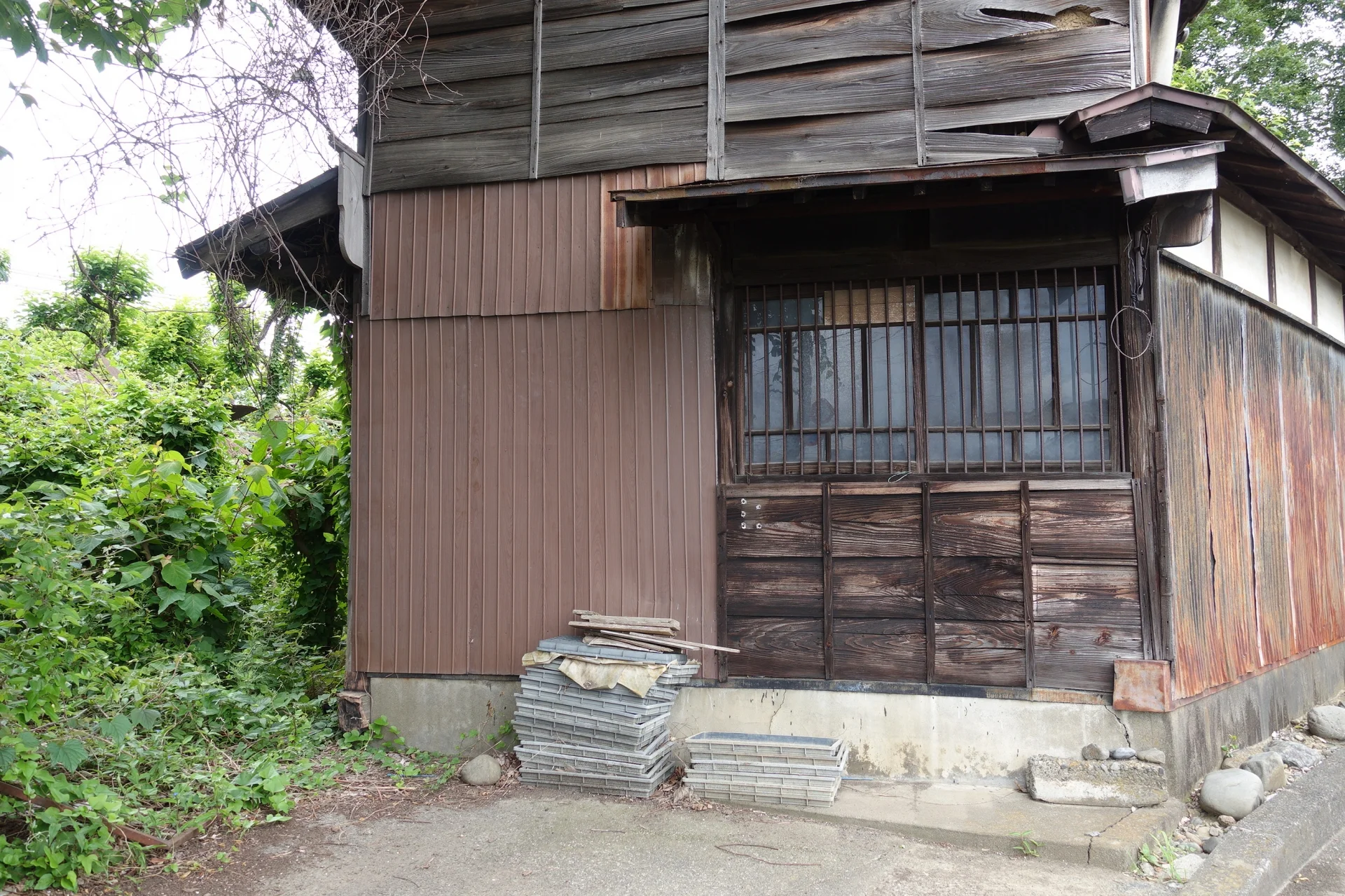 外壁の板が反り、草木に囲まれた古い木造の空き家