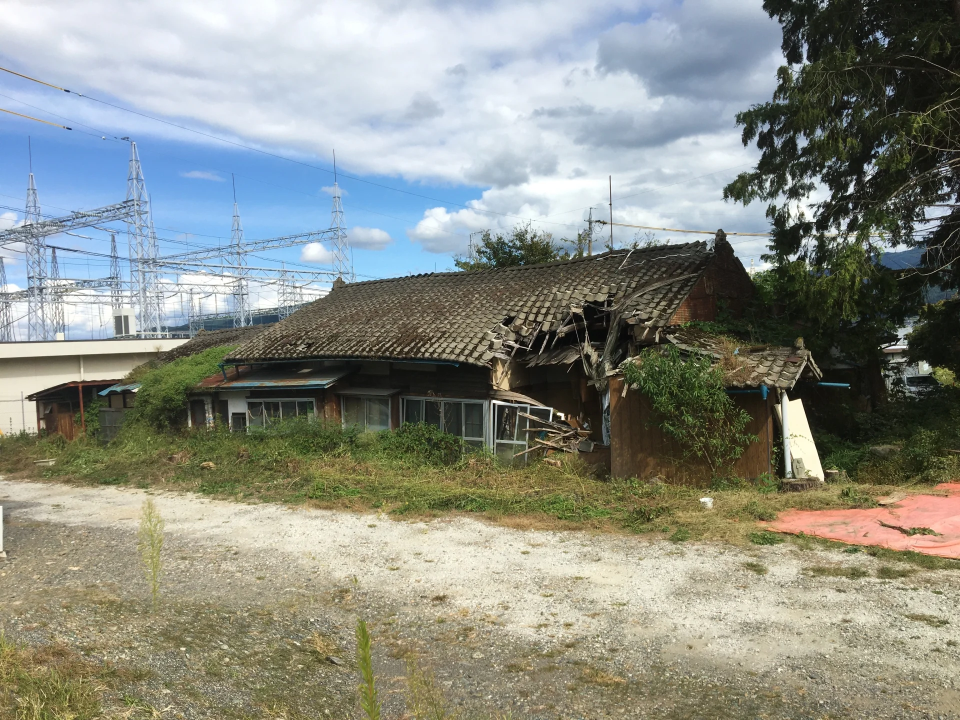 屋根の一部が崩れ落ち、雑草に囲まれた平屋の古い空き家