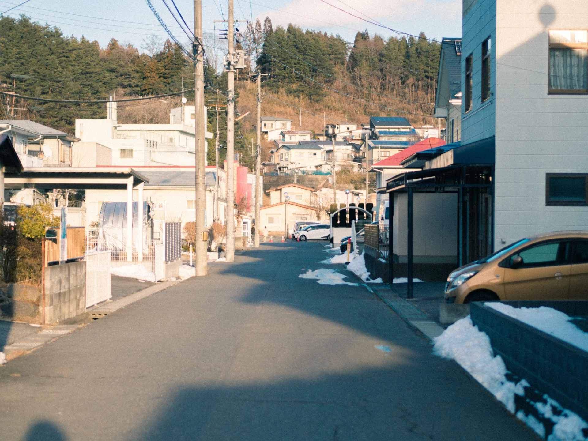 道路脇に雪が残る、山すその地方の住宅街（士別市の空き家の無償譲渡のイメージ）