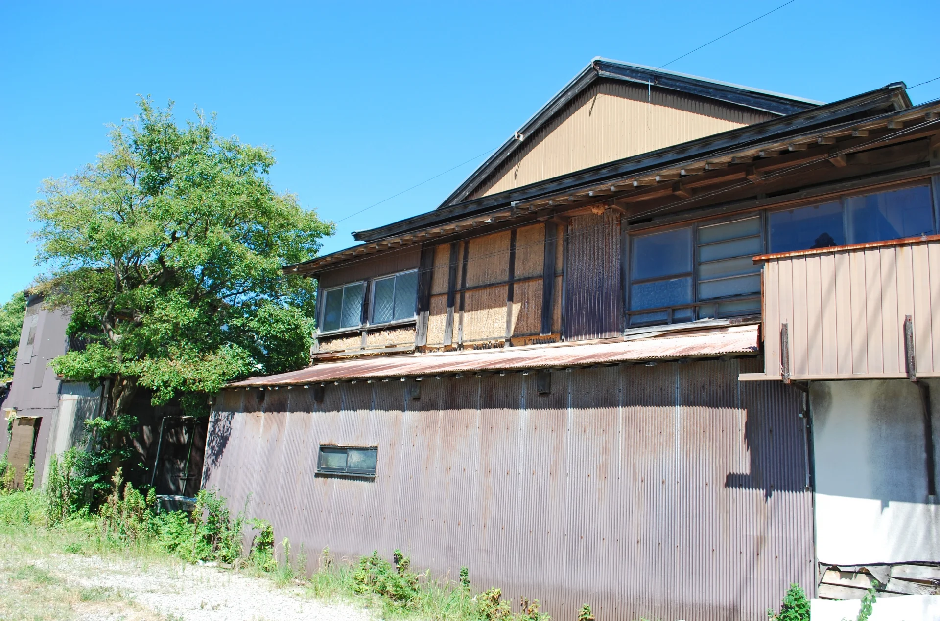 青空の下に建つ、外壁の傷んだ木造2階建ての古い空き家(神戸で空き家を無料で手放すイメージ)