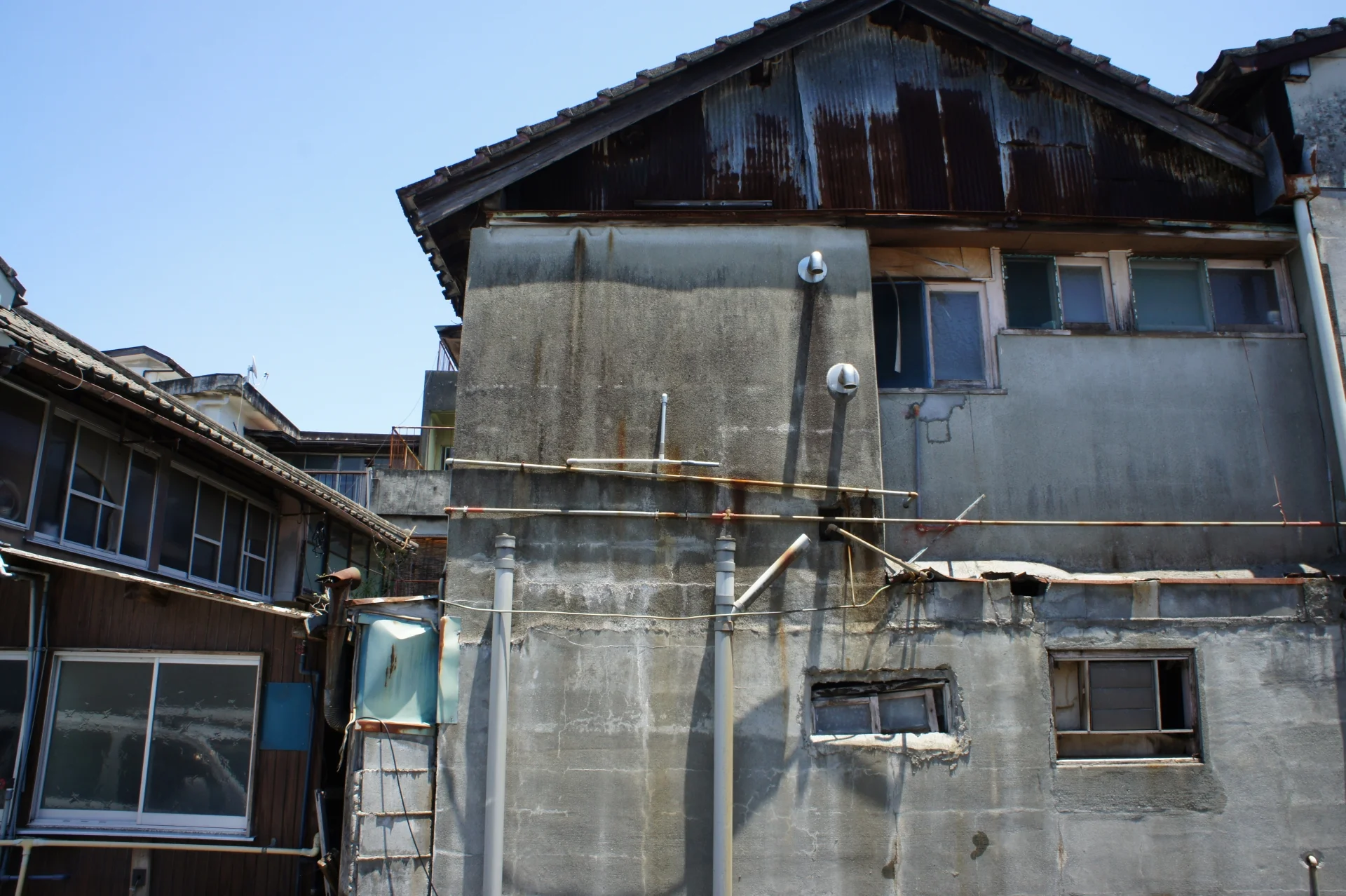 青空の下で、外壁のくすんだ古い2階建ての家を見上げた様子(富山市で空き家を無料で手放すイメージ)