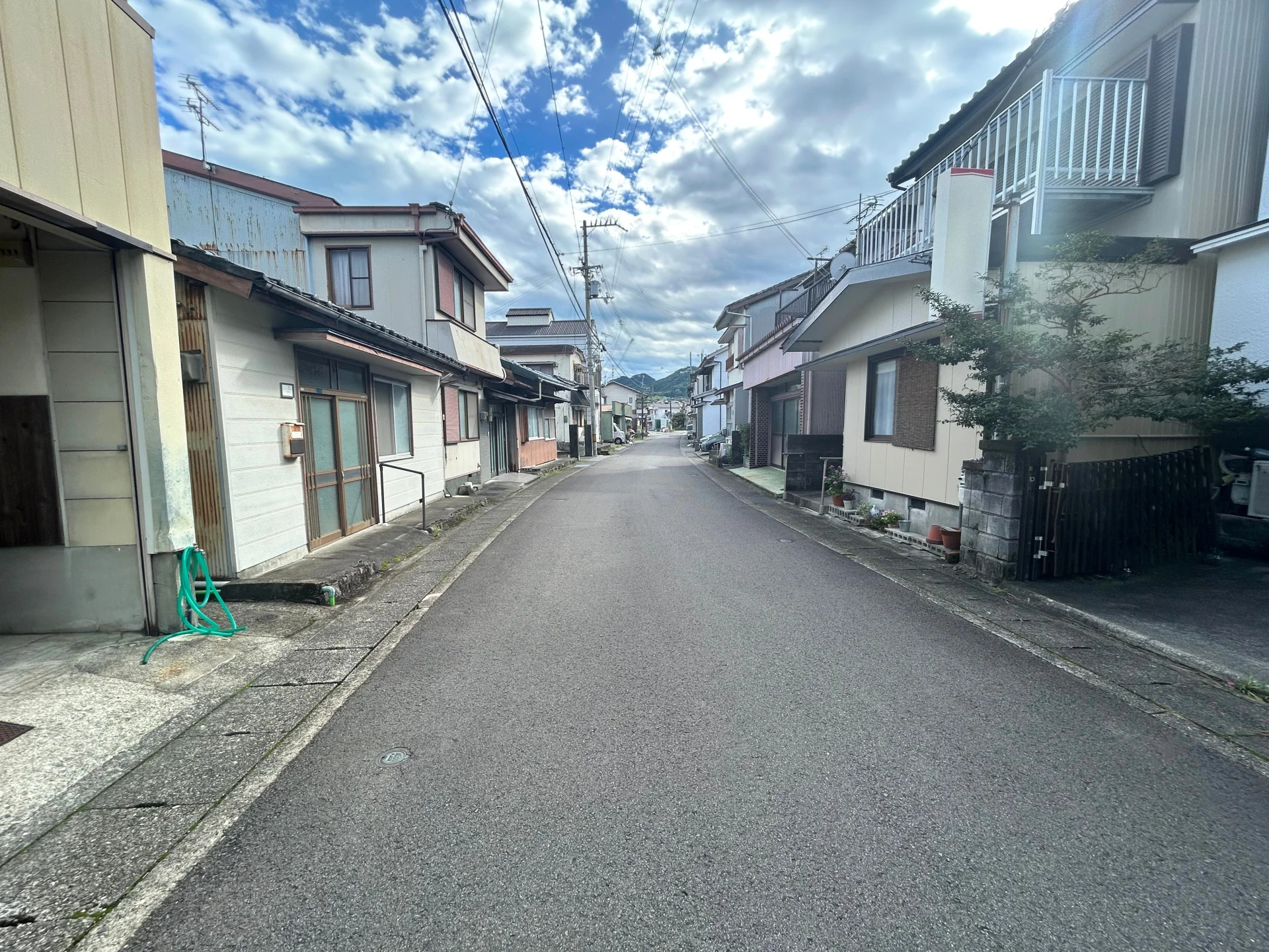 山を背に古い木造の戸建てが道の両側に並ぶ地方都市の住宅街(佐伯市の家の手放し方のイメージ)